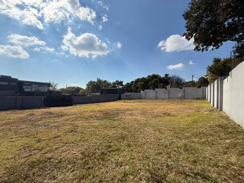 A vacant residential plot featuring a grass lawn, enclosed by perimeter walls with installed electric fencing.