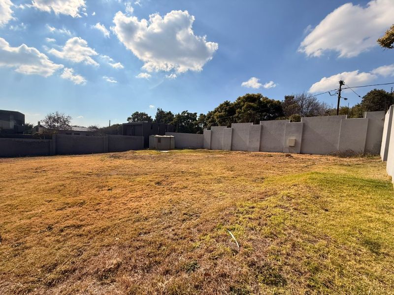 A spacious, level vacant residential plot enclosed by high perimeter walls with integrated electric fencing and a small utility shed.