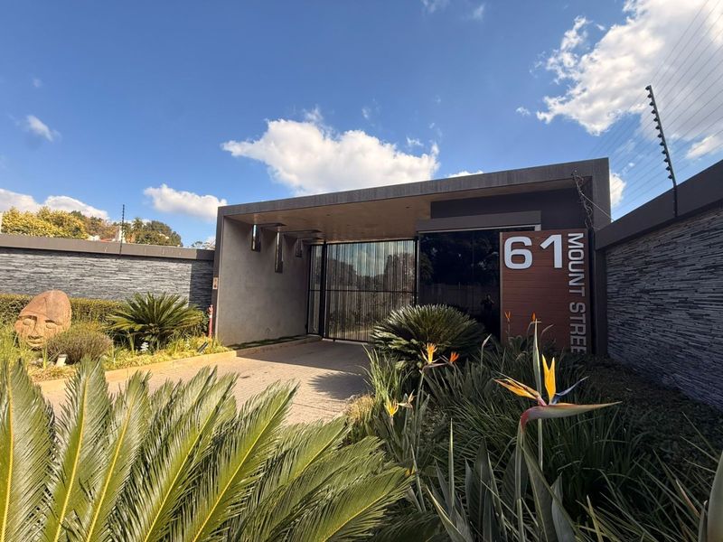 Modern residential entrance featuring a secure electric gate, stone-clad boundary walls, electric fencing, and a well-maintained landscaped garden.