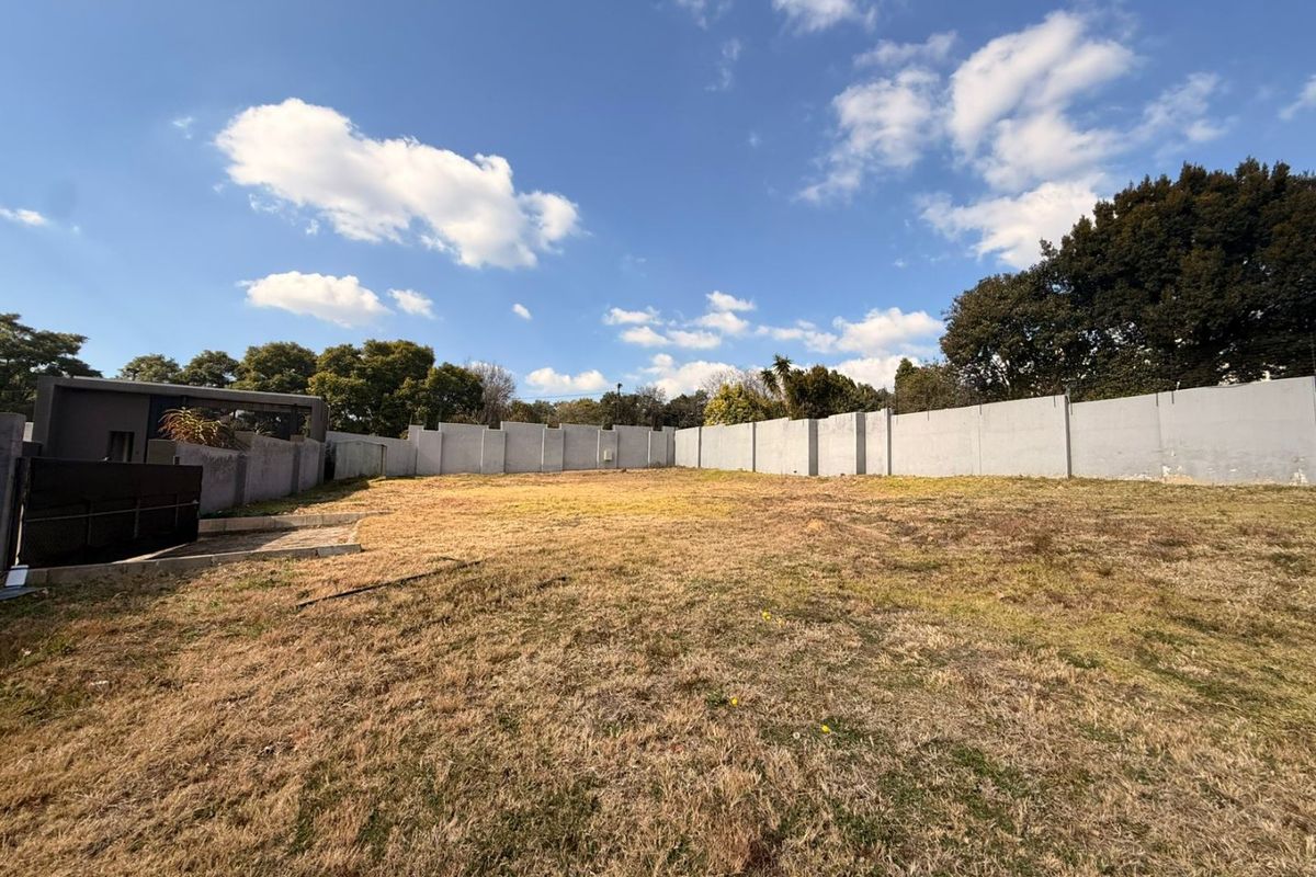 A vacant residential plot featuring a large open grass area enclosed by a concrete perimeter wall.