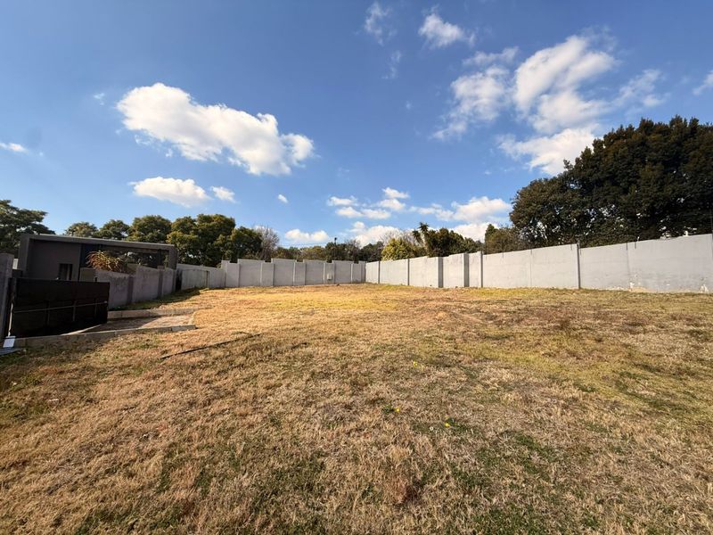 A vacant residential plot featuring a large open grass area enclosed by a concrete perimeter wall.