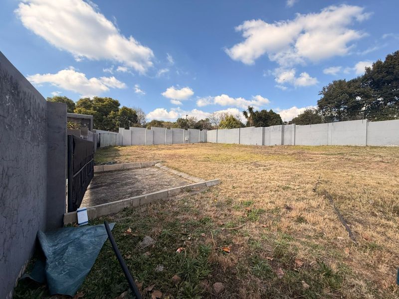 A vacant residential plot featuring a perimeter wall, a small concrete slab, and a metal gate, offering a clear space for development.