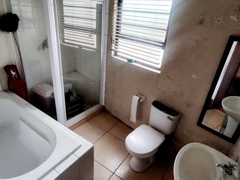A dated bathroom featuring a built-in bathtub, separate shower enclosure, toilet, and pedestal basin, requiring significant cosmetic updates and wall repairs.