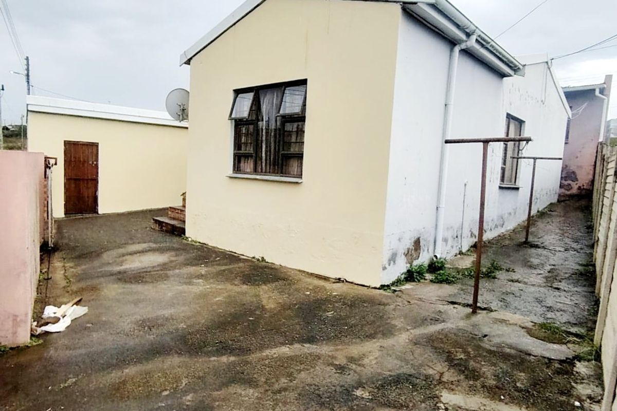 Rear exterior view of the property showing a concrete yard, metal washing lines, and the side elevation of the house with visible wall weathering.