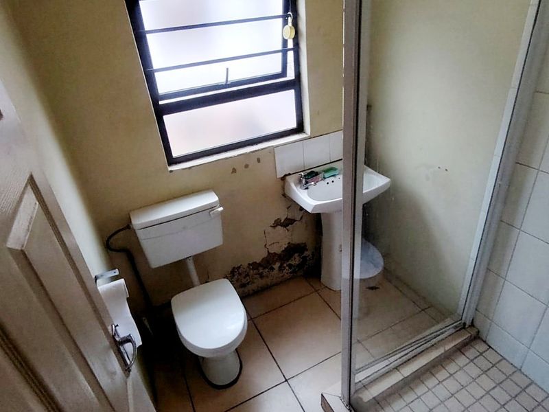 A compact bathroom featuring a pedestal basin, toilet, and shower enclosure, currently requiring significant wall repairs and cosmetic updates.