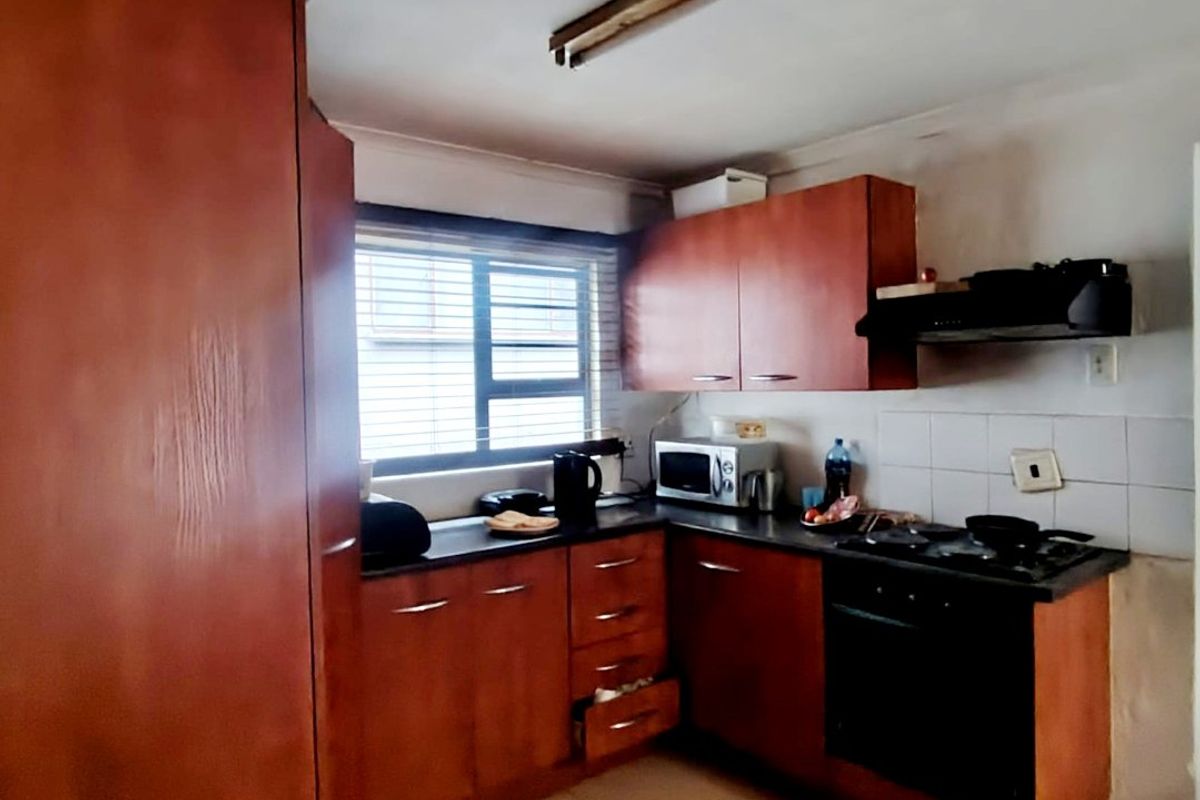 A functional kitchen featuring wood-tone cabinetry, built-in oven and hob, tiled backsplash, and tiled flooring, requiring some cosmetic updates to modernize the space.