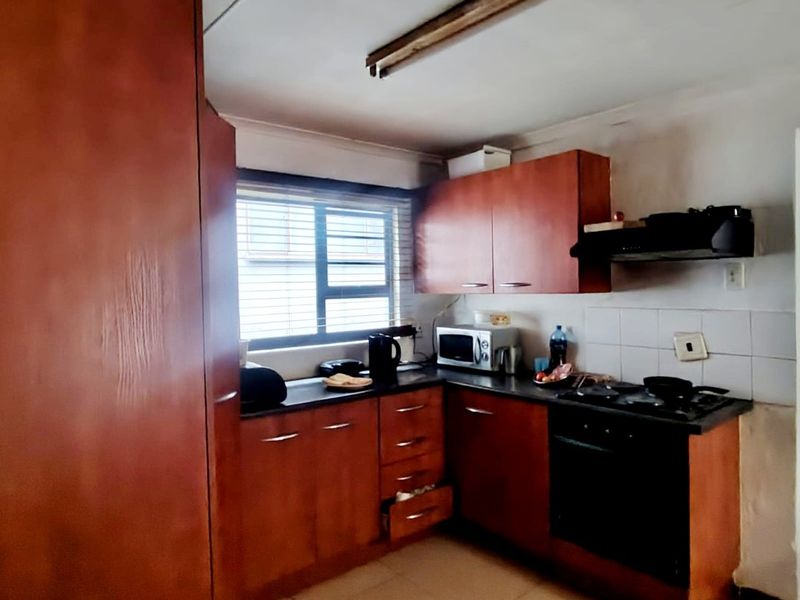 A functional kitchen featuring wood-tone cabinetry, built-in oven and hob, tiled backsplash, and tiled flooring, requiring some cosmetic updates to modernize the space.