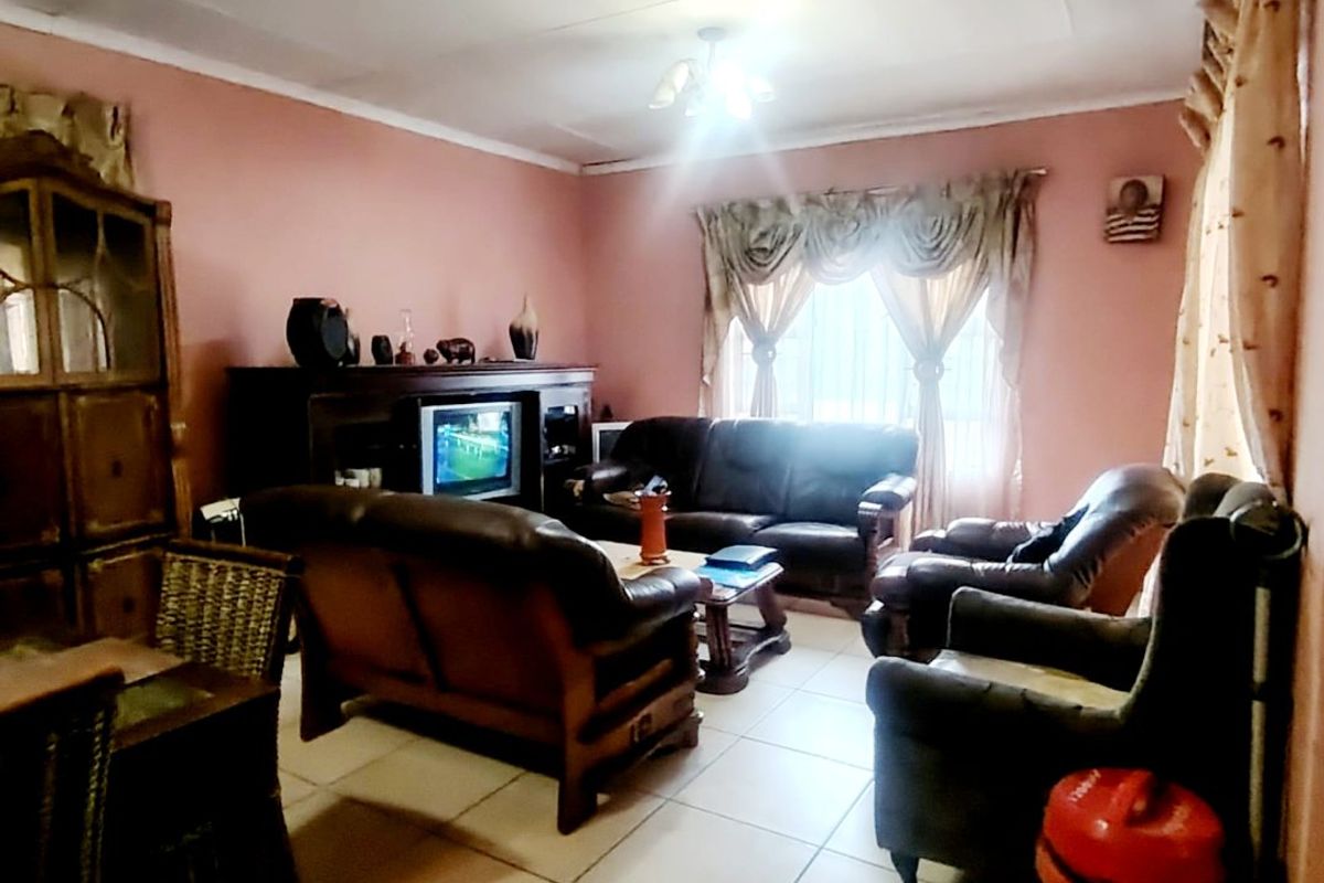 A living room featuring tiled flooring and standard ceiling finishes, currently furnished with a lounge suite.