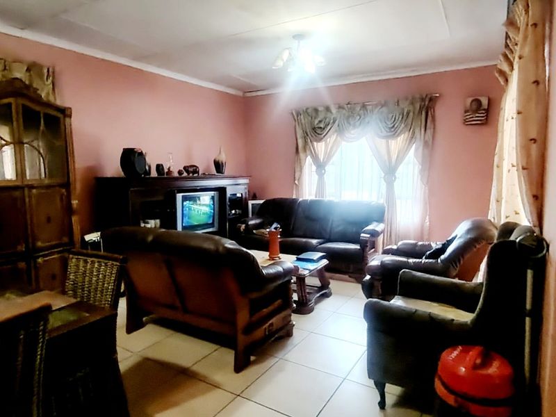 A living room featuring tiled flooring and standard ceiling finishes, currently furnished with a lounge suite.