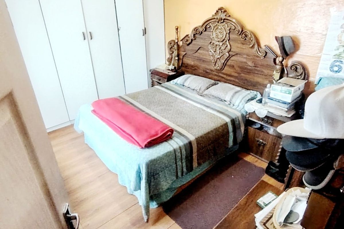 A bedroom featuring built-in cupboards and laminate flooring, currently showing signs of wear on the wall surfaces.