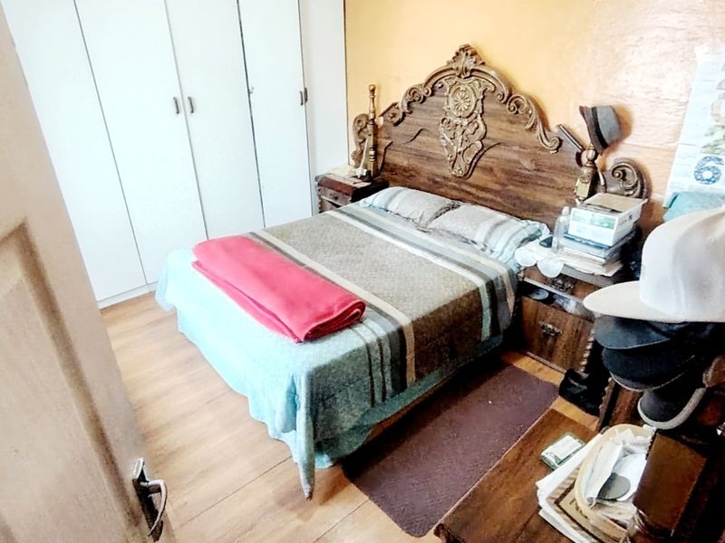 A bedroom featuring built-in cupboards and laminate flooring, currently showing signs of wear on the wall surfaces.