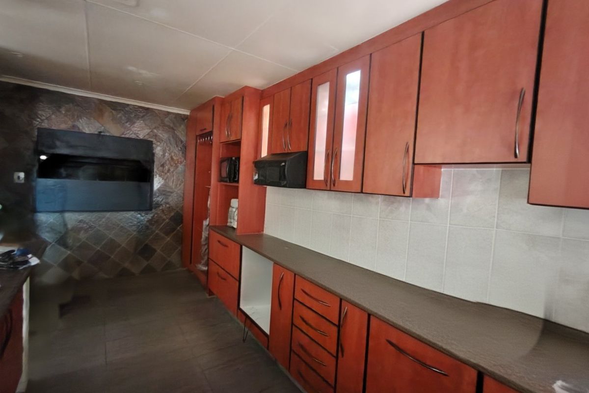 A functional kitchen featuring extensive built-in cabinetry, laminate countertops, tiled backsplash, and a built-in indoor braai area.