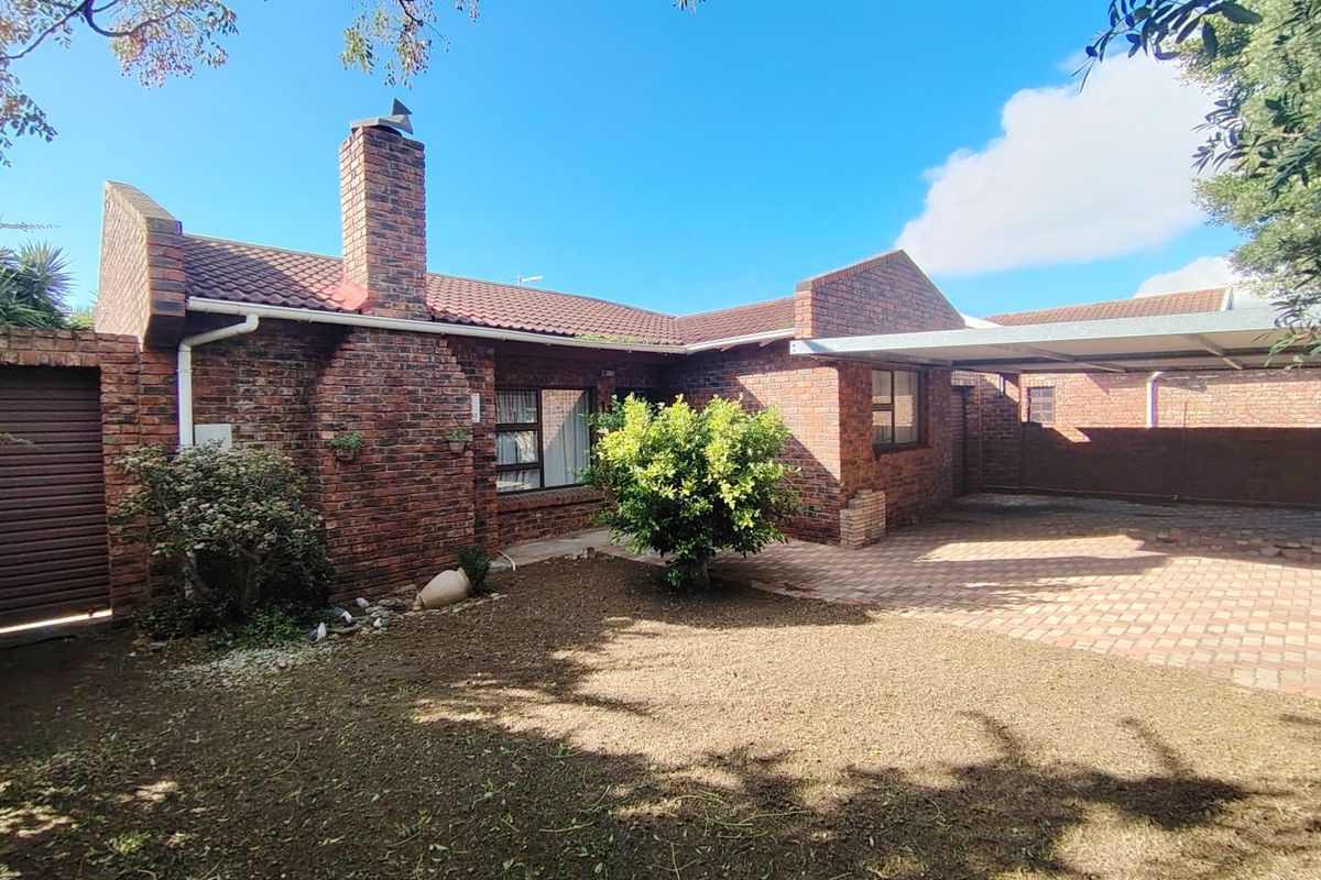 Rear view of a face-brick house featuring a tiled roof, brick chimney, paved driveway area, and a covered carport.