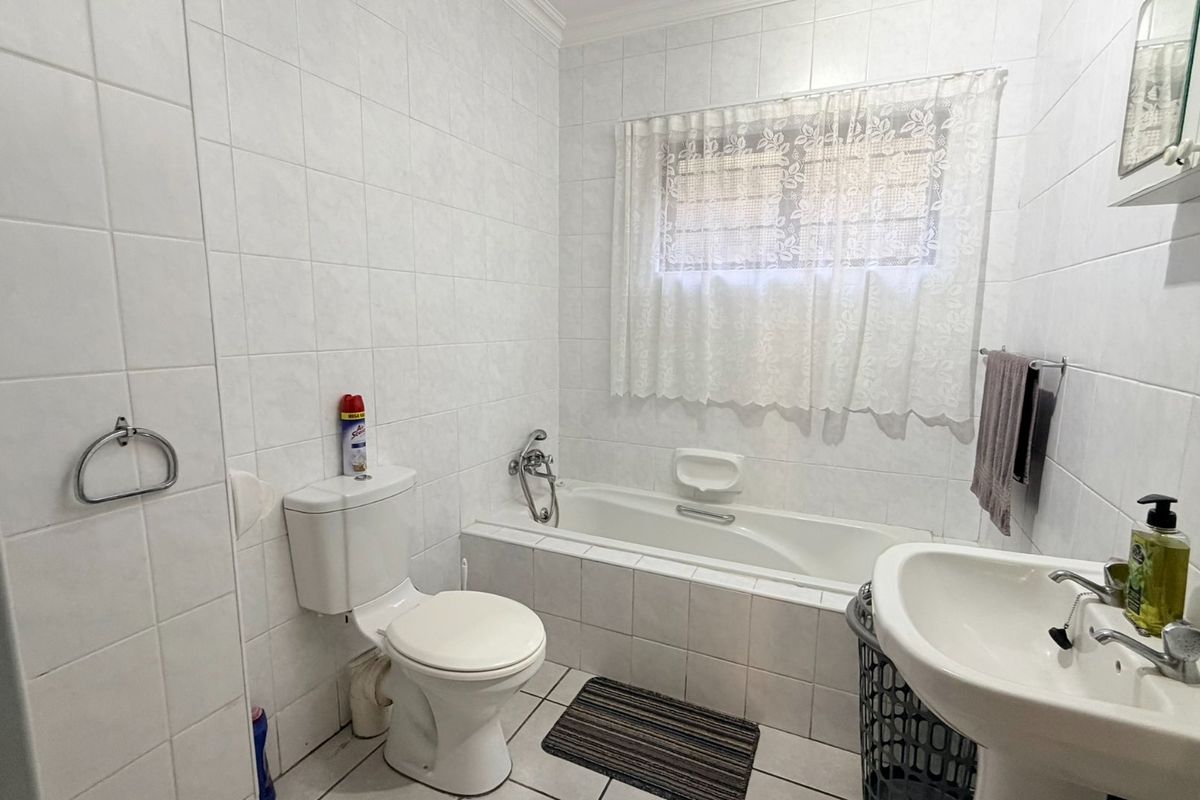 A functional bathroom featuring a bathtub, pedestal basin, and toilet with neutral white wall and floor tiling.