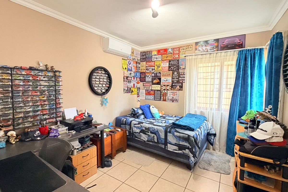 A bedroom featuring tiled flooring, an air conditioning unit, and security bars on the window, providing a functional living space.