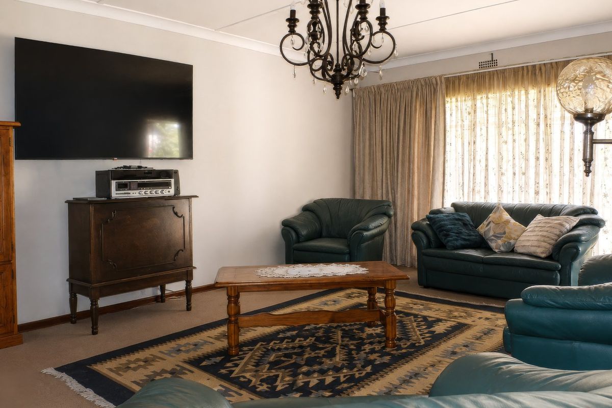 A comfortable living room featuring neutral walls, carpeted flooring, and a classic chandelier, providing a functional space for relaxation.
