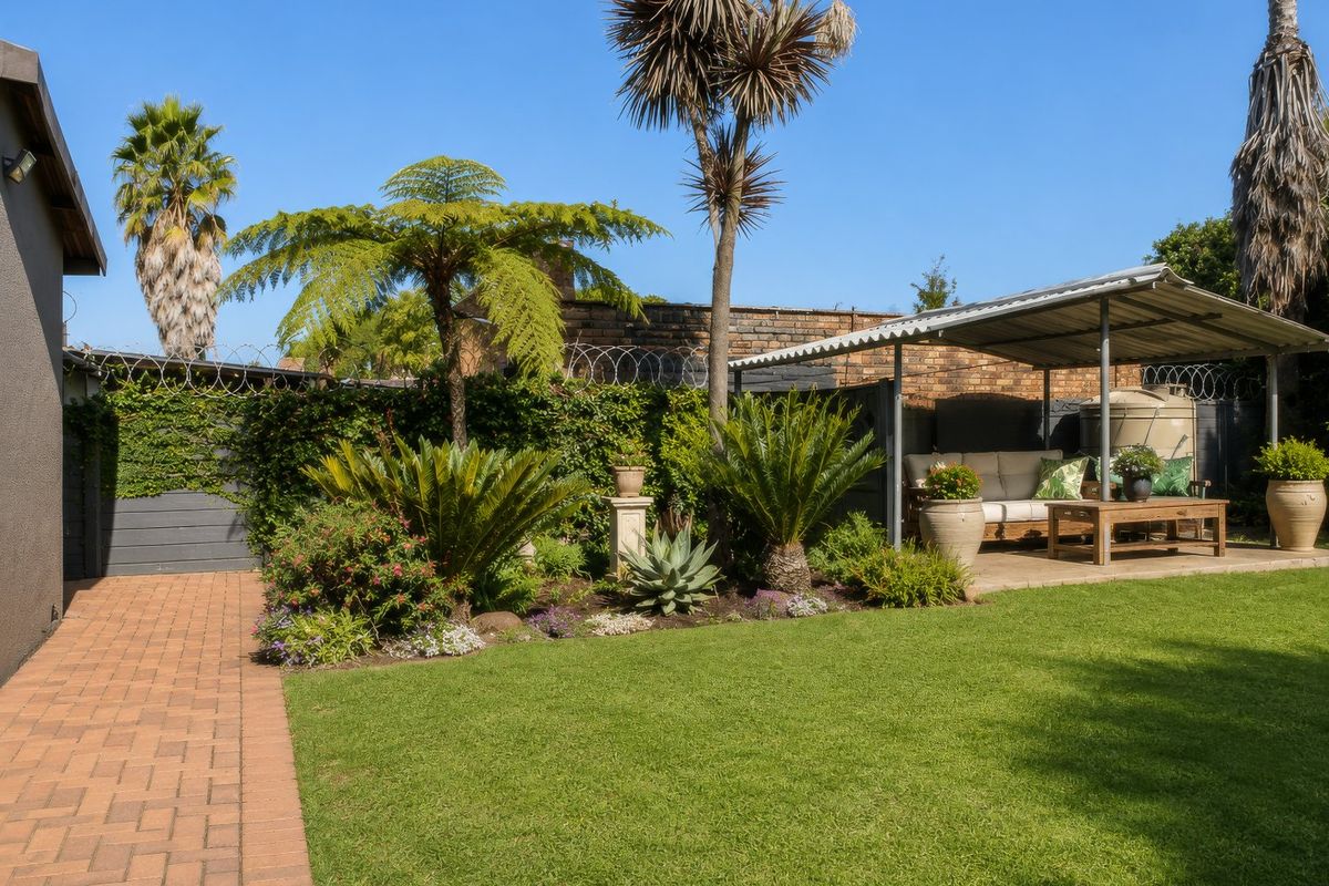A well-maintained rear garden featuring a brick paved walkway, established landscaping, and a covered patio area with a water tank.