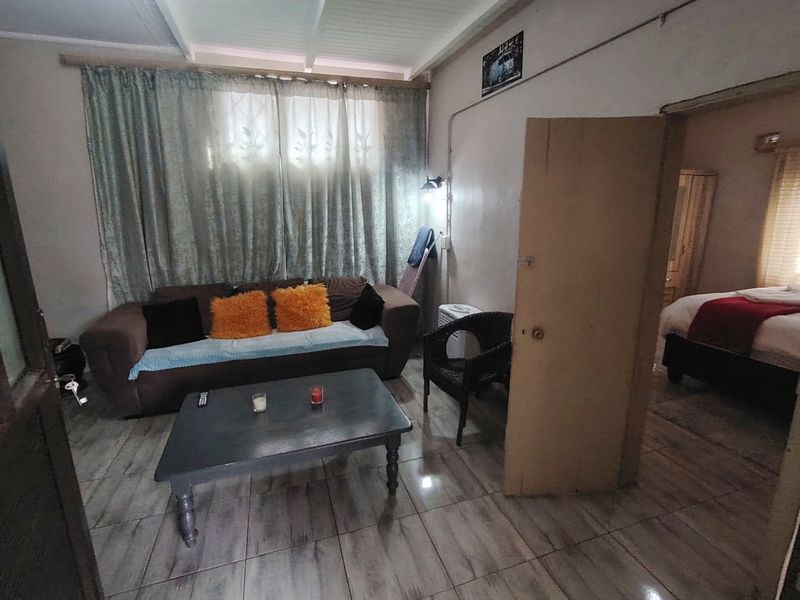 A living area featuring tiled flooring and exposed beam ceilings, with an adjacent bedroom visible through the doorway.