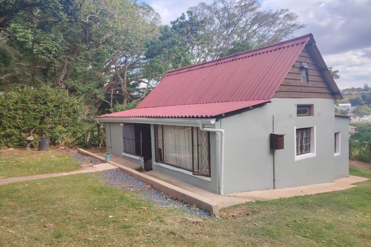 A rear view of a cottage-style house featuring a red corrugated metal roof, timber gable detailing, and security bars on the windows.