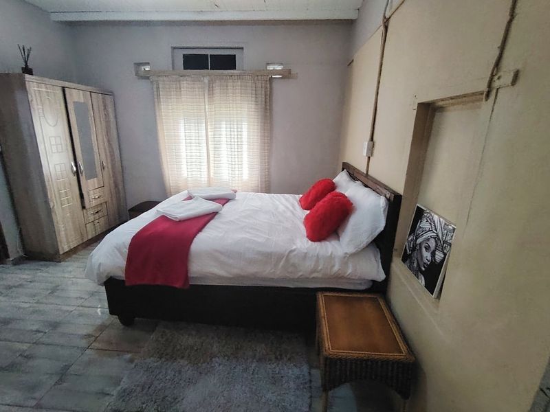 A bedroom featuring tiled flooring, exposed ceiling beams, and a recessed wall niche, requiring cosmetic updates to improve the overall finish.