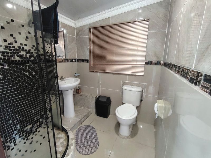 A functional bathroom featuring a pedestal basin, a corner shower enclosure with mosaic tile accents, and full-height wall tiling.