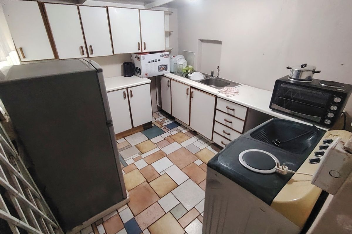 A dated kitchen featuring white cabinetry, a stainless steel sink, and multi-colored tiled flooring, offering potential for a modern renovation.