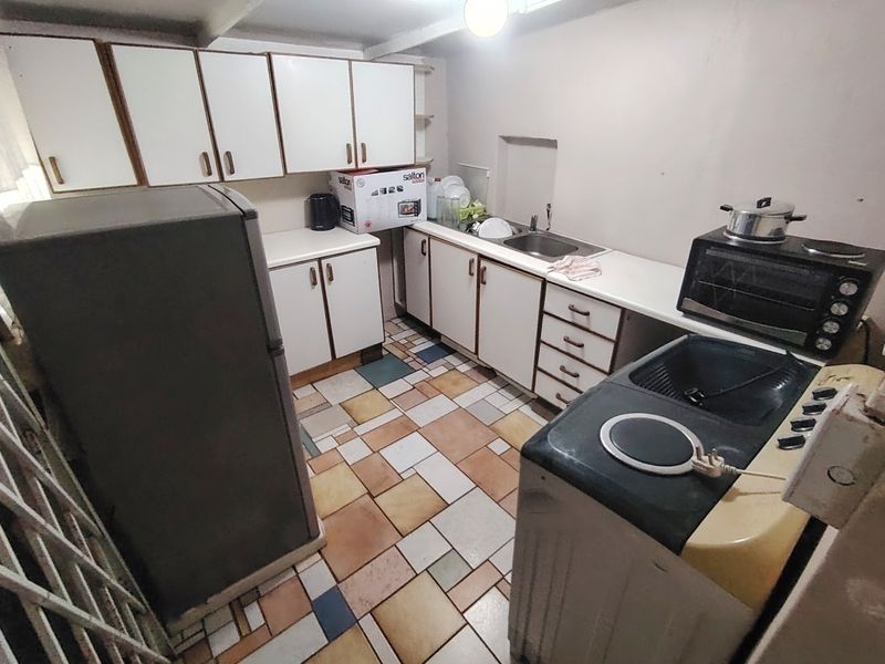 A dated kitchen featuring white cabinetry, a stainless steel sink, and multi-colored tiled flooring, offering potential for a modern renovation.