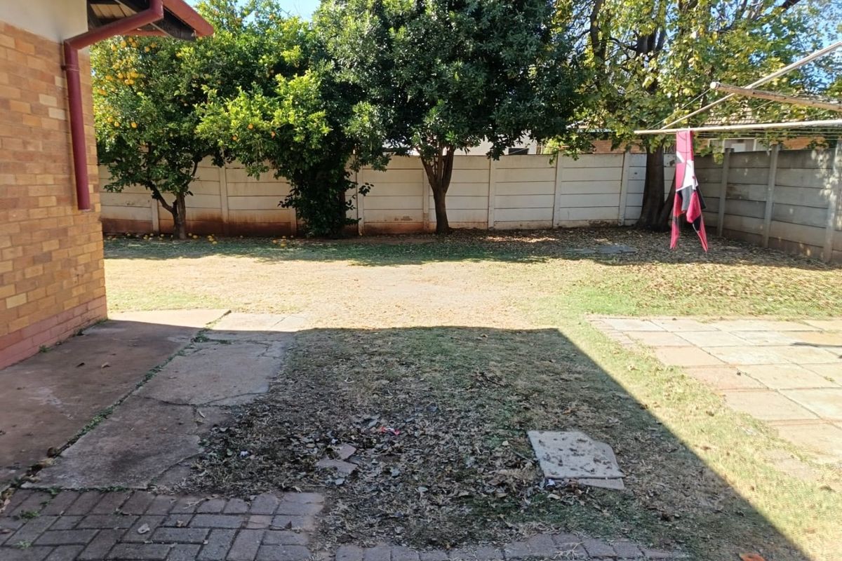 A rear garden area featuring a paved patio, brick exterior wall, and precast concrete boundary fencing, requiring landscaping and maintenance.