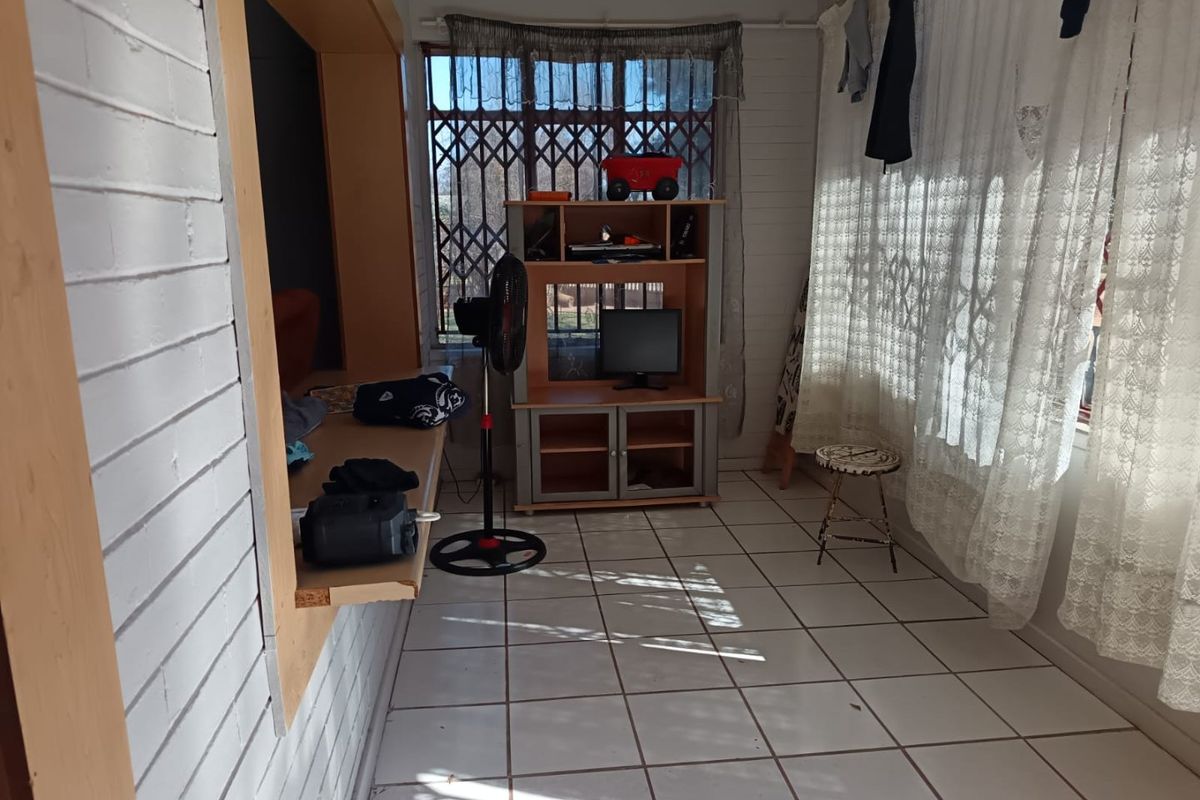 A living area featuring tiled flooring and painted brick walls, with natural light entering through a window protected by a security gate.