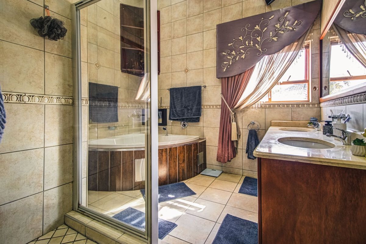 A spacious bathroom featuring a corner bathtub, a glass-enclosed shower, and a double vanity with stone countertops and wood-finish cabinetry.