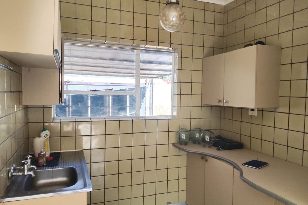 A dated kitchen featuring original wall tiles, laminate countertops, and built-in cabinetry, offering significant potential for a modern renovation.