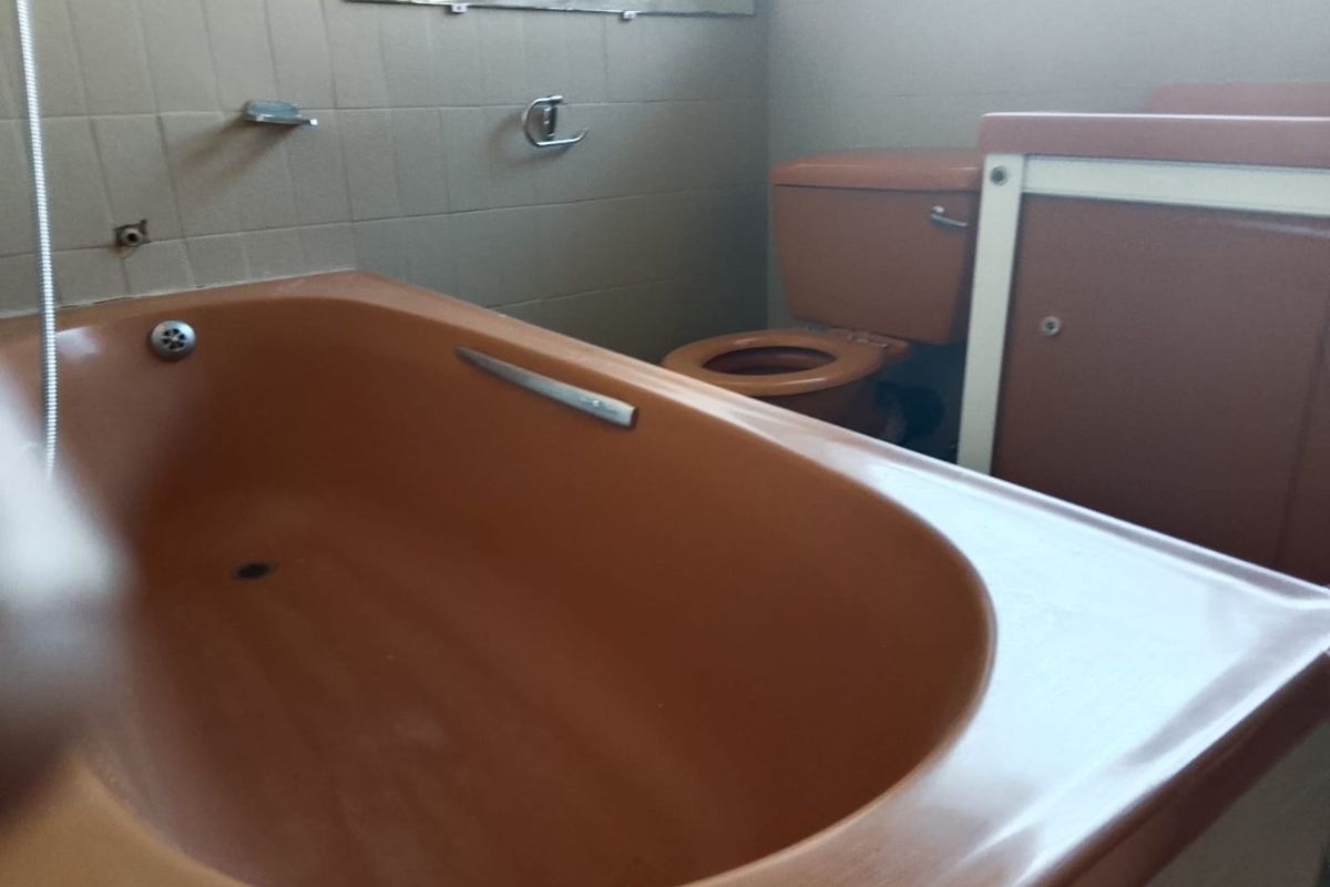 A dated bathroom featuring original brown sanitaryware, including a built-in bathtub and toilet, with tiled walls and a vanity unit.