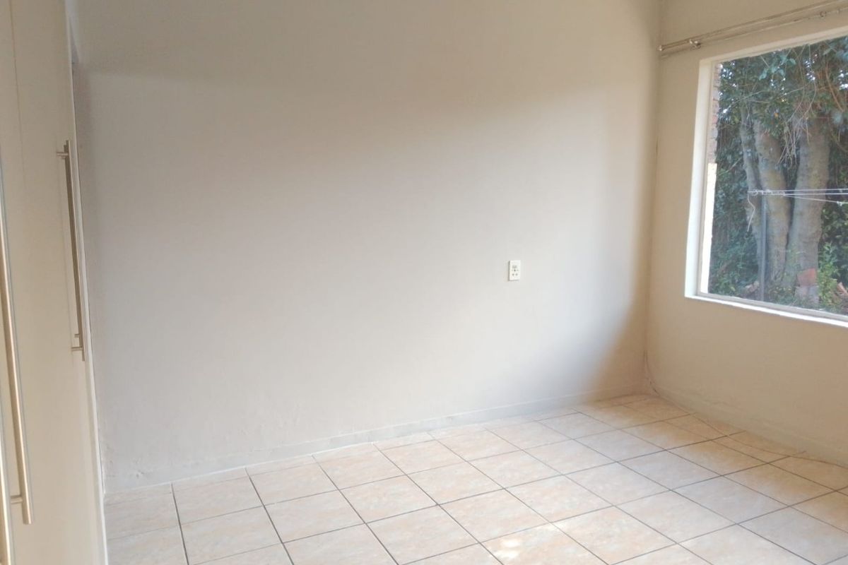 A vacant bedroom featuring neutral wall paint, tiled flooring, and a built-in cupboard, offering a clean canvas for personalization.