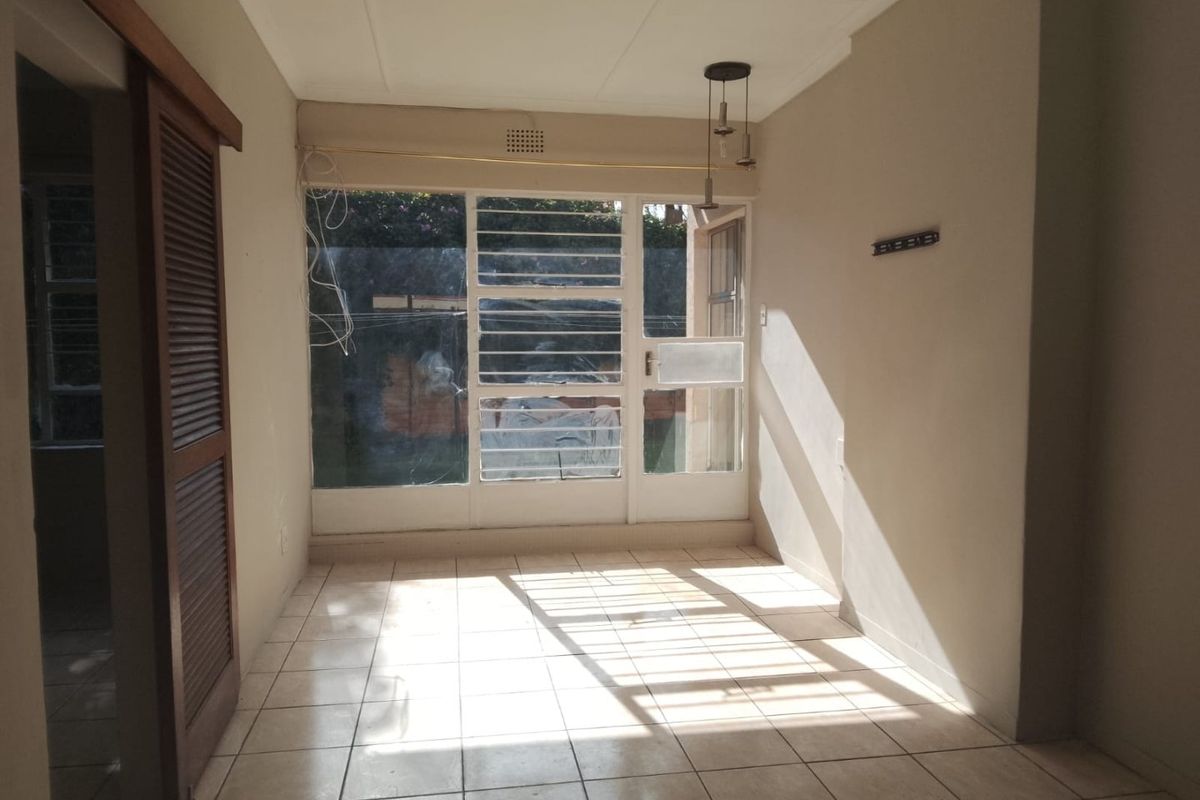 A bright, empty living area featuring tiled flooring, a sliding door with security bars, and natural light, offering a blank canvas for renovation.