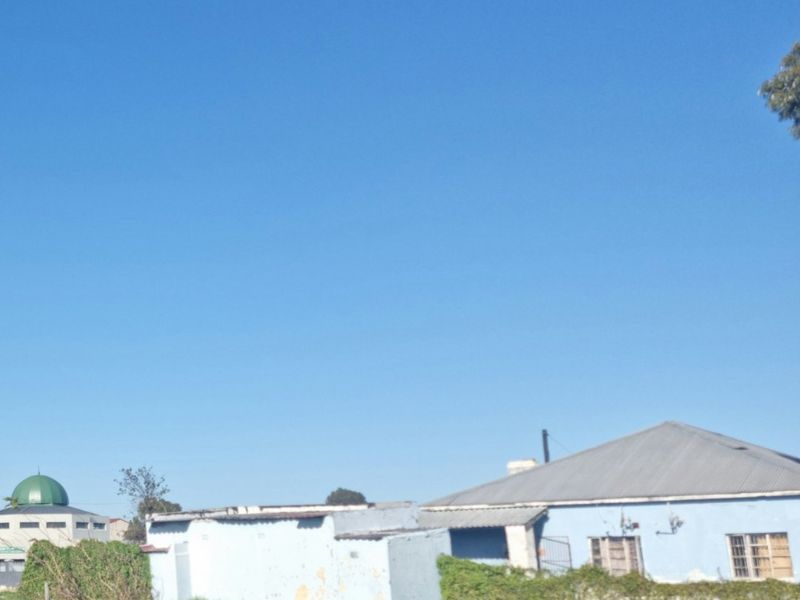 A street-facing view of a single-story residential property featuring a corrugated metal roof and light blue masonry walls with visible signs of weathering.