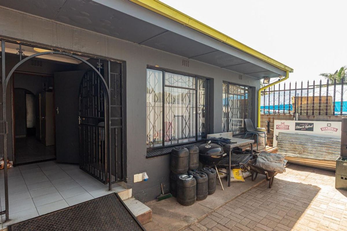 Rear exterior view of the commercial property featuring a paved courtyard, security gates, and window bars, with access to the main building entrance.