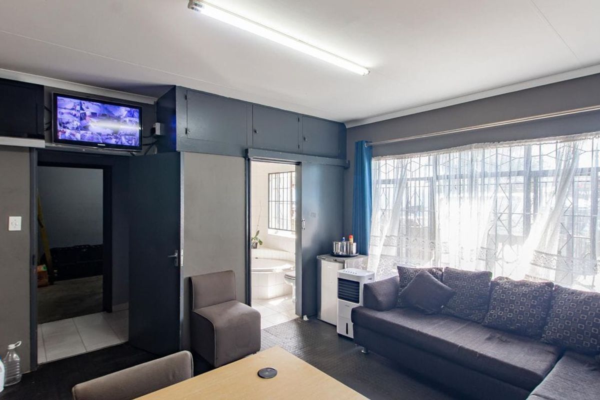 A functional living area featuring built-in overhead cabinetry, large windows with security bars, and direct access to an adjoining room.
