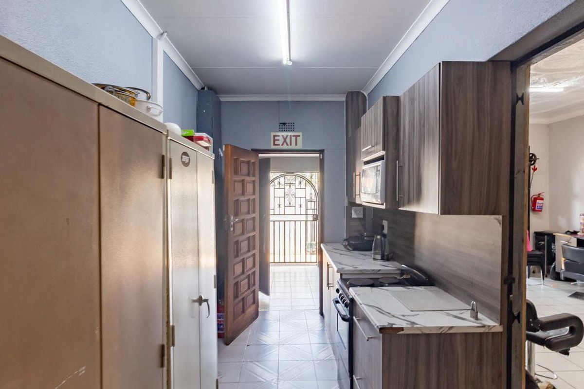 A functional kitchen area featuring wood-grain cabinetry, marble-effect countertops, built-in cooking appliances, and direct access to an exterior security gate.