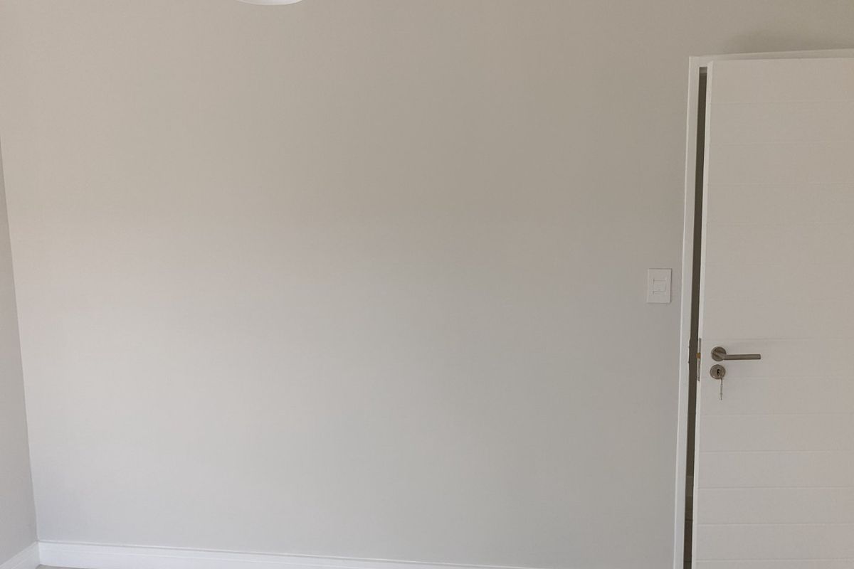 A clean, neutral-toned bedroom featuring tiled flooring, a modern internal door, and a simple light fixture, presenting a blank canvas for interior design.