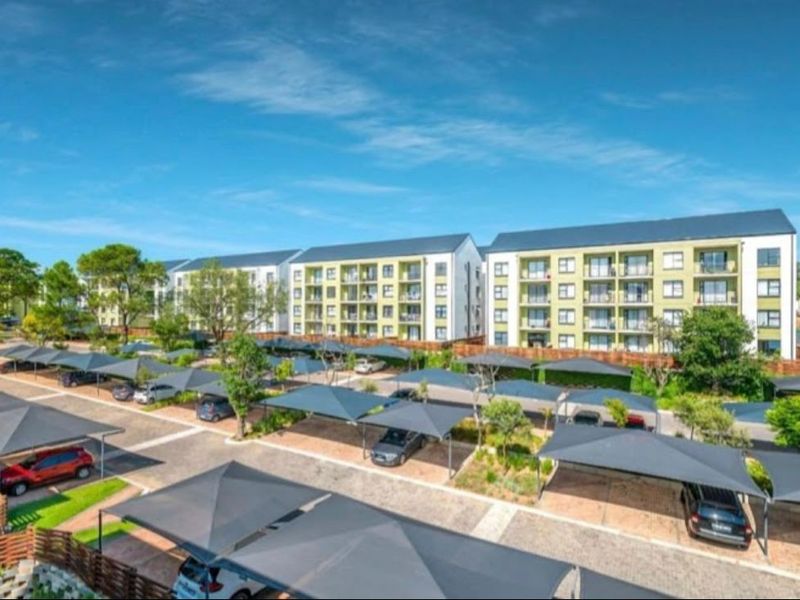 Exterior view of a modern apartment complex featuring extensive paved parking areas with shade cloth carports and landscaped grounds.