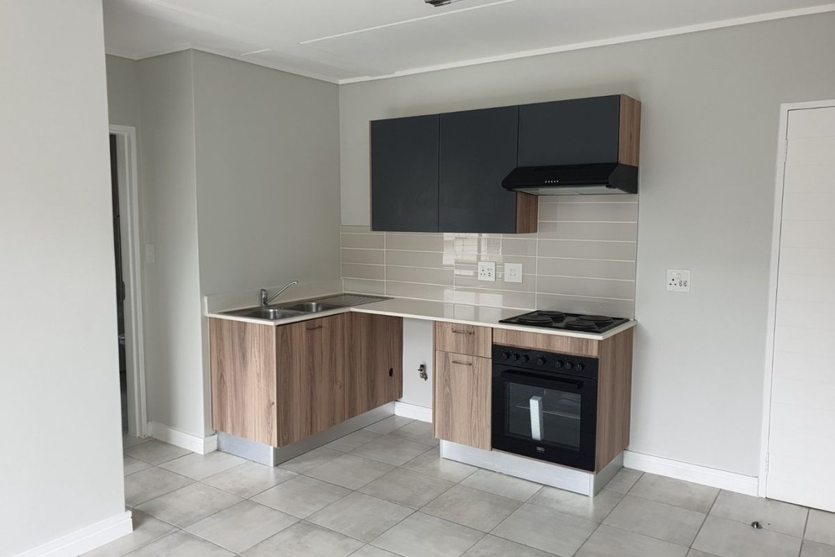 A clean, modern kitchen featuring wood-grain lower cabinets, dark upper cupboards, built-in oven, hob, extractor fan, and neutral tiled flooring.