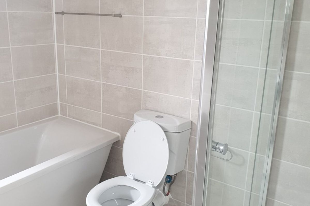 A clean, modern bathroom featuring a bathtub, separate shower enclosure, and neutral ceramic tiling throughout.