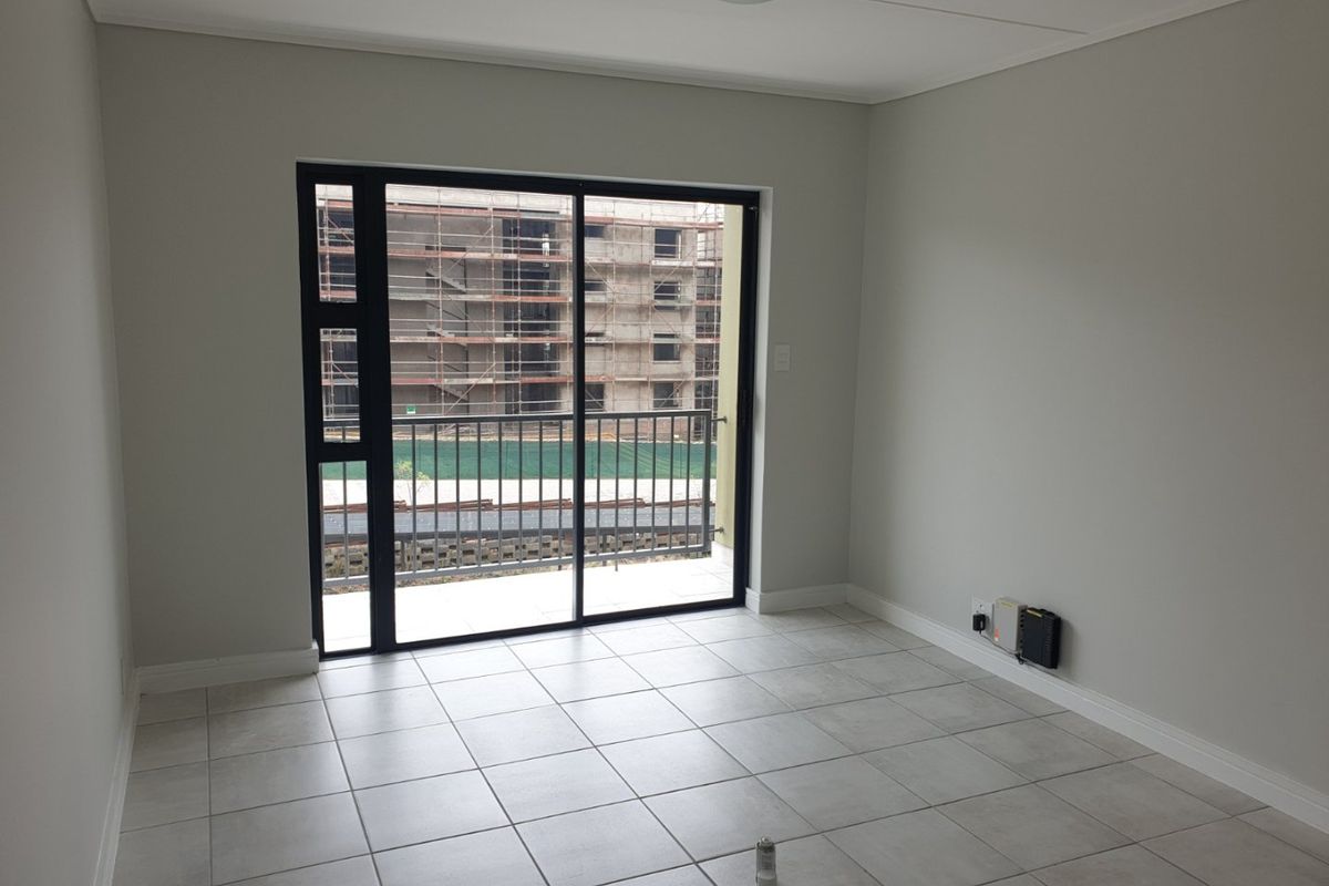 A bright, empty living area featuring neutral tiled flooring and a large sliding glass door that opens onto a balcony.