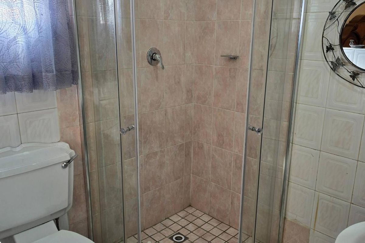 A functional bathroom featuring a curved glass shower enclosure, pedestal basin, and toilet with dated ceramic wall and floor tiling.