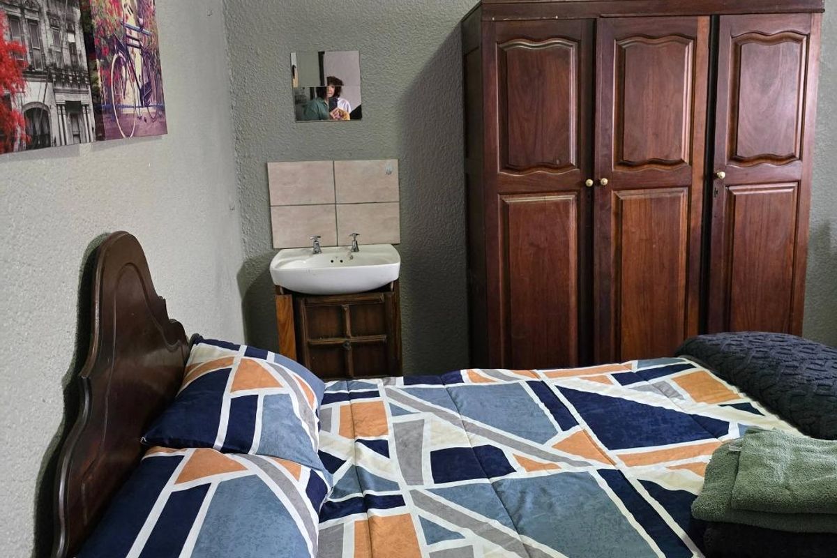 A bedroom featuring a built-in vanity basin with a tiled splashback and a ventilation grille on the wall.