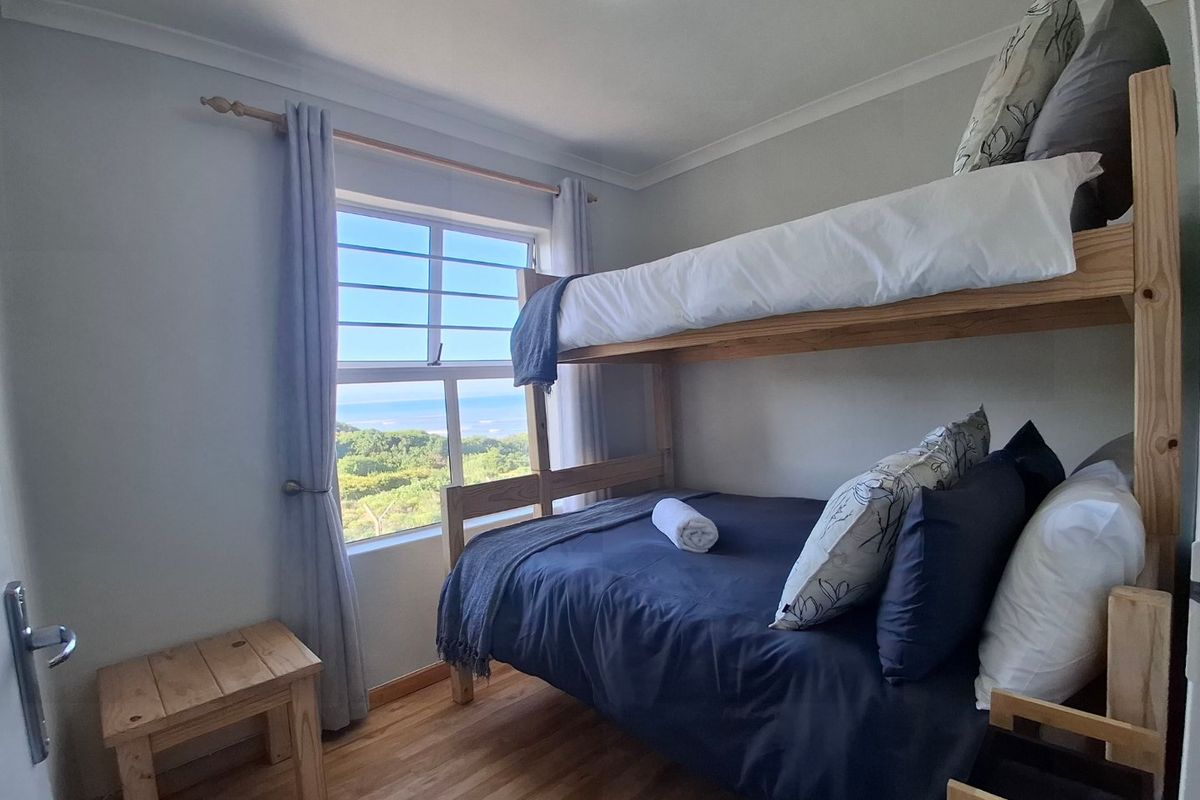 A cozy bedroom featuring laminate flooring, cove cornicing, and a window with security bars offering scenic coastal views.