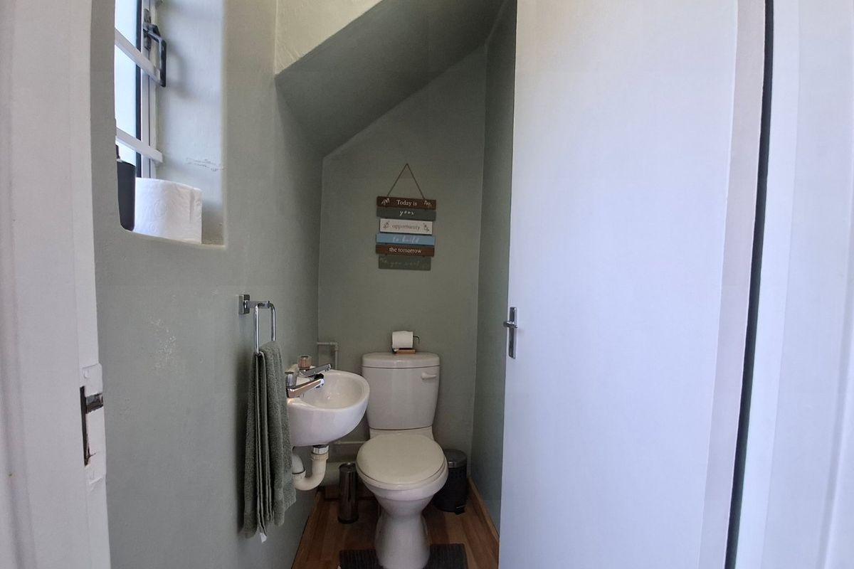 A compact guest bathroom featuring a wall-mounted basin, toilet, and laminate flooring, situated under a staircase with a small window for natural light.