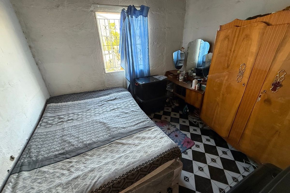 A bedroom featuring tiled flooring and security bars on the window, requiring cosmetic updates to the wall finishes.