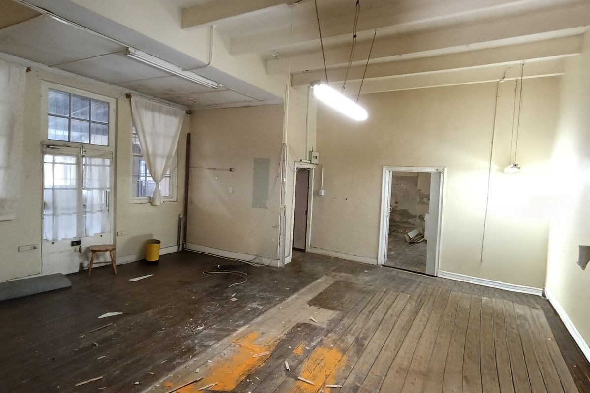 An empty, fixer-upper living area featuring exposed timber ceiling beams, original timber flooring, and multiple access points, requiring significant renovation and cosmetic updates.