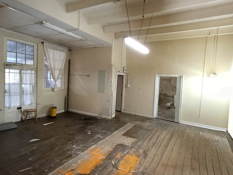An empty, fixer-upper living area featuring exposed timber ceiling beams, original timber flooring, and multiple access points, requiring significant renovation and cosmetic updates.
